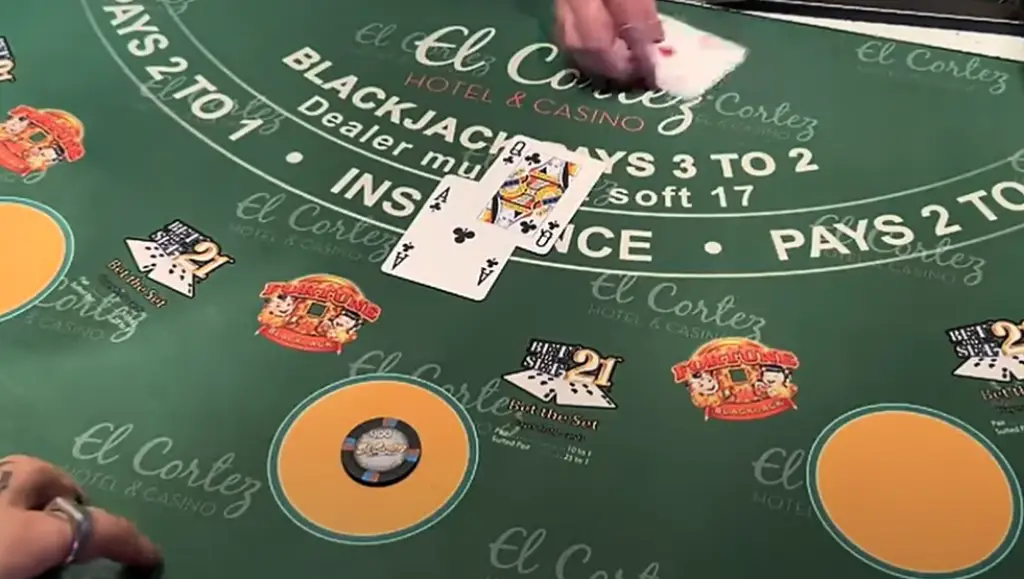 a live blackjack table at the El Cortez Hotel & Casino. The table features clear markings for blackjack rules, such as "Blackjack Pays 3 to 2," "Dealer Must Hit Soft 17," and "Insurance Pays 2 to 1." A dealer is visible dealing cards, with a hand showing a King of Spades and an Ace of Clubs—a blackjack hand. The table design includes colorful logos and betting circles.